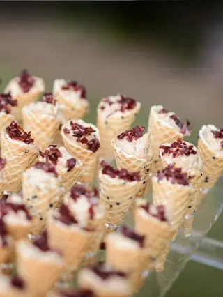 Cucuruchos de barquillo rellenos de crema salada con crujiente por encima, servidos en soporte de cristal en un cóctel