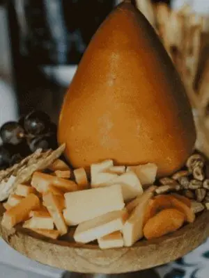 Queso de forma cónica con dados de queso curado, orejones, pistachos y uvas sobre una tabla de madera para picoteo